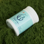 Qingshi Tablet bottle with teal label lying on green textured fabric 